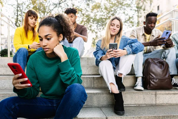 Young addicted people using smart phone outdoors. Group of friends holding smartphone device chatting on social media app. Youth and technology concept.
