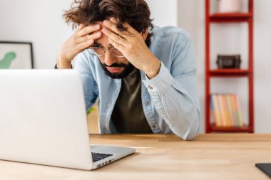 Yorgun genç adam dizüstü bilgisayardan kötü haberler okuyor..