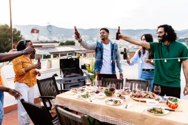Bir grup çok ırklı ve çeşitli yetişkin arkadaş dışarıda bir terasta birlikte öğle yemeği yerken bira ile kadeh kaldırıyorlar. Gençler yaz partisinde birayla tezahürat yapıyor.