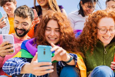 Farklı genç LGBT dostları açık havada birlikte akıllı telefon kullanıyor. İletişim ve LGBTİ topluluk kavramı.