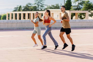 Şehir parkında birlikte koşan üç genç arkadaşın yan görüntüsü. Uzayı metin için kopyala. Fitness insanları konsepti.