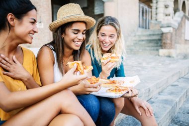 Üç genç İtalyan kadın dışarıda birlikte oturmuş pizza yiyorlar. İtalya 'da tatilin tadını çıkaran çeşitli kadın turistler. Seyahat ve arkadaşlık kavramı.