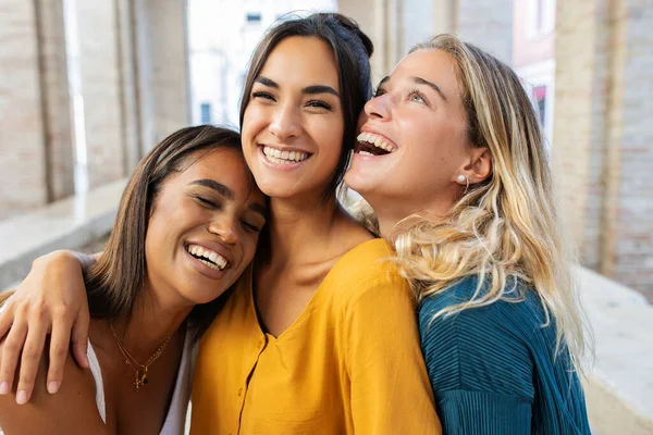 Three happy woman laughing together outdoors. Portrait of diverse female friends having fun enjoying day off at city street in Italy.
