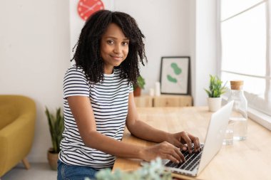 Evde dizüstü bilgisayarda çalışan Afrikalı Amerikalı genç bir kadının portresi. İş yerinde oturan gülümseyen Brezilyalı kadın. Teknoloji konsepti.