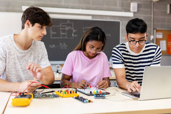 Diverse young teenage student friends learning together to build electronic circuit at high school