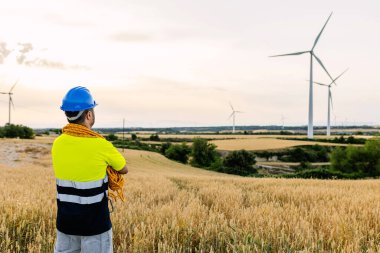 Rüzgâr türbini çiftliğine bakan genç bir işçinin arka görüntüsü. Gelecek ve yenilenebilir enerji kavramı.