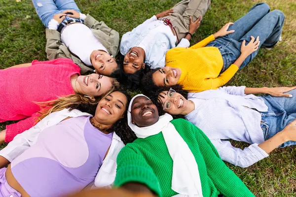 Happy group of women lying on circle on grass taking selfie portrait at park. Empowerment, people, female friendship and youth community concept.