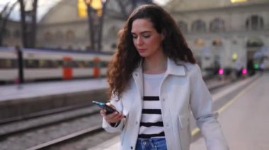 Tren istasyonunda akıllı telefon kullanan genç ve güzel bir kadın.