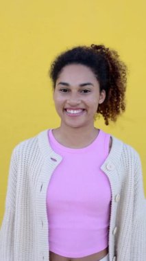 Sarı arka planda kameraya gülümseyen neşeli genç Latin Amerikalı kadın. Kıvırcık kızın dikey portresi pozitif hissediyor, dişlek gülümsemesini dışarıda gösteriyor..