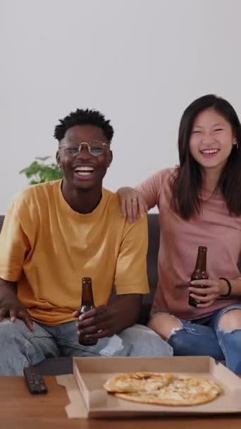 家庭でテレビを見ている多民族の幸せな友人 10代の若者のグループは 週末の休みにピザを食べてビールを飲むという社交的な集まりを楽しんでいます 友情とレジャーのコンセプト — ストック動画