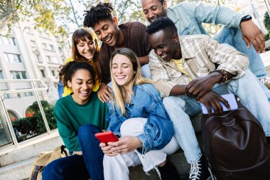 Bin yıllık çeşitli arkadaşlar cep telefonlarını şehir merdivenlerinde otururken kullanıyorlar. Şehir hayatı, teknoloji ve arkadaşlık kavramı.
