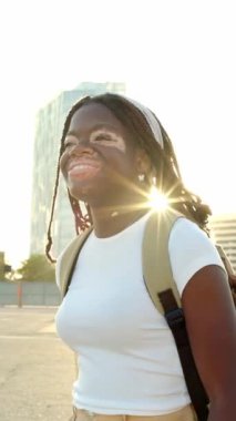 Vitiligo 'su olan genç bir genç kız gün batımında şehrin arka planında mutlu mesut yürüyor. Dışarıda özgüvenle yürüyen Afrikalı bir kadın var. Gençlik kültürü ve çeşitlilik kavramı. Yavaş çekim görüntüleri