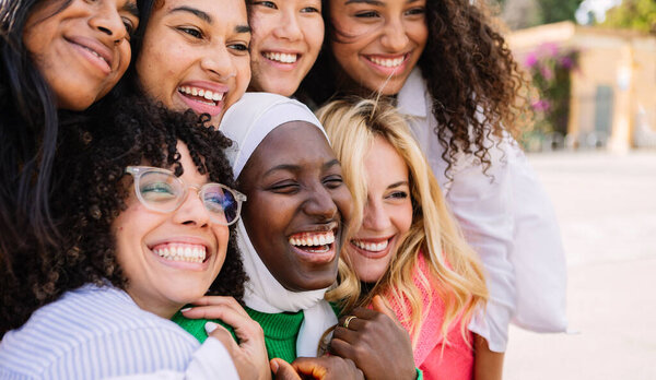 Diverse group of women having fun together outdoors. Multiracial girls laughing while hugging each other at city street. Female friendship concept