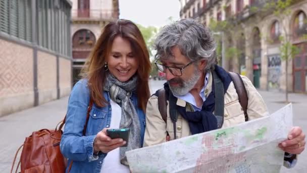 バルセロナでの散歩を楽しんでいる間 街の地図を保持しているハッピーシニア大人の観光カップル 旅行休暇中に携帯アプリで観光スポットを探している中年男性と女性 — ストック動画