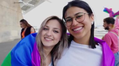 Gay onur festivali kutlamalarında kameraya gülümseyen ve öpüşen lezbiyen çiftin portresi. LGBTQ topluluk kavramı.