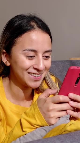 若い美しいヒスパニック系ラテン系の少女は リビングルームのソファーで休んでいる間 スマートフォンデバイスにメッセージを入力します 技術ライフスタイルコンセプト — ストック動画