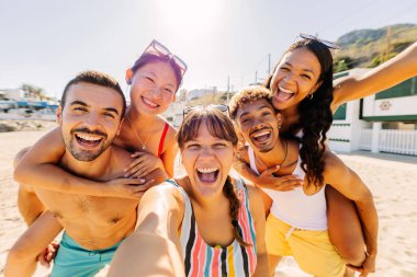 Çeşitli insanlar birlikte selfie çektirirken ve telefon ile sahilde yaz tatilinin tadını çıkarırken eğleniyor. Arkadaşlık ve tatil kavramı.