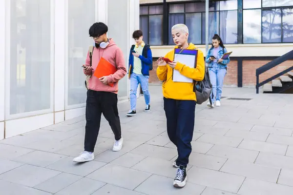 stock image College students using mobile phone after classes while leaving university building campus.