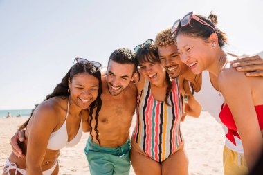 Genç bir grup insan yaz tatilinin tadını çıkarırken sahilde birbirlerine sarılıp eğleniyorlar. Arkadaşlık ve tatil kavramı.