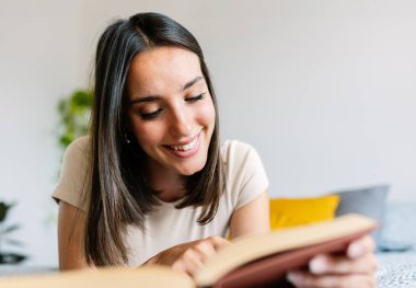 Kitap okurken yatakta yatan mutlu genç bir kadının yakın plan portresi. Boş zaman aktivite konsepti.