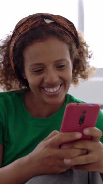 Mutlu genç Afrikalı kadın evde akıllı telefon kullanarak eğleniyor. Dikey HD ekran görüntüleri.