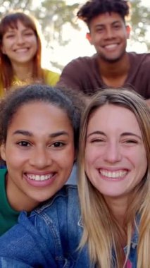 Dışarıdaki kameraya gülümseyen dört mutlu gencin portresi. Milenyum çeşitliliği olan arkadaşlar birlikte şehir caddesinde oturuyorlar. Arkadaşlık ve gençlik yaşam tarzı kavramı. Dikey HD video