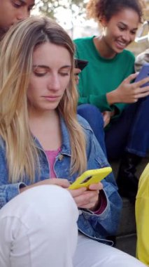 Milenyum gençleri dışarıda cep telefonu kullanıyor. Çok ırklı arkadaş grubu akıllı telefon uygulamasında sohbet ediyorlar. Teknoloji yaşam tarzı. Dikey HD video.