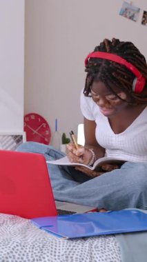 Vitiligo 'su olan Afrikalı genç bir bayan odasında yatağında oturan dizüstü bilgisayarla internetten ders çalışıyor. Eğitim, e-öğrenim ve gençlik kavramı.