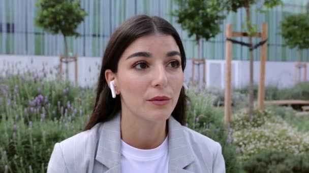 Ung Affärskvinna Pratar Mobilen Med Trådlösa Hörlurar Medan Sitter Utomhus — Stockvideo