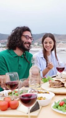 Dikey video. Genç bir grup mutlu arkadaş ev terasında akşam yemeğinin tadını çıkarıyorlar. Çok ırklı erkekler ve kadınlar doğum günlerini kutlamak için akşam yemeğinin tadını çıkarıyorlar. Yaz partisi konsepti.