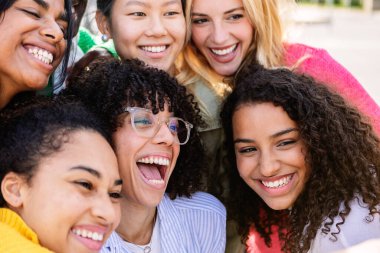 Açık havada birlikte gülen bir grup mutlu kızın yakın görüntüsü. Kadın arkadaşlığı kavramı, çok ırklı genç kadınlarla şehir sokaklarında eğleniyor..