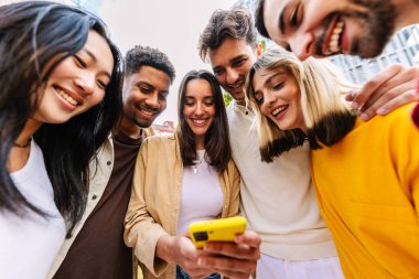 Şehir caddesinde cep telefonu kullanan bir grup mutlu genç. Milenyum çeşitliliği cep telefonu uygulamasında sosyal medyadan keyif alan arkadaşlar. Teknoloji yaşam tarzı ve gençlik toplumu kavramı.