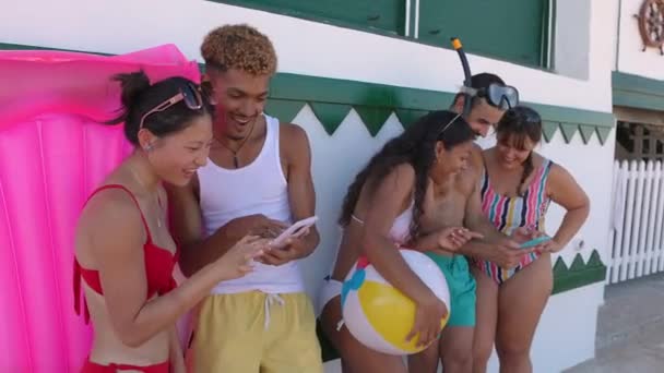 ビーチの壁に携帯電話が傾いている水着の多様な人々の若いグループ 技術と夏のコンセプト — ストック動画
