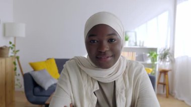 POV mutlu genç Afrikalı kadın evde laptoptan video dinliyormuş. İslami başörtüsü takmış genç bir kız arkadaşıyla internette konuşuyor. Eğitim ve gençlik kavramı.