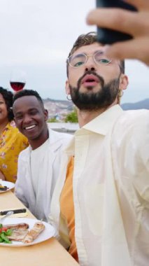 House Terrace 'da barbekü partisinde eğlenen mutlu genç arkadaş grubunun dikey videosu. Milenyum neşe dolu erkek ve kadınlar kutlama sırasında telefonla selfie çekiyorlar..