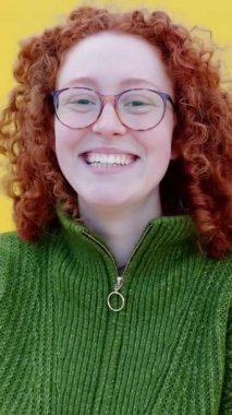 Sarı arka planda gülümseyen genç kızıl kadının dikey HD portresi. Gençlik toplumu ve halk kavramı.