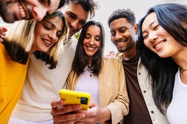 Şehir caddesinde cep telefonu kullanan bir grup mutlu genç. Milenyum çeşitliliği cep telefonu uygulamasında sosyal medyadan keyif alan arkadaşlar. Teknoloji yaşam tarzı ve gençlik toplumu kavramı.
