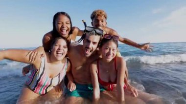 Suda şişme minderleri olan çok ırklı arkadaşların komik grup portresi sahilde yaz tatilinin tadını çıkarıyor. Tatil yaşam tarzı ve arkadaşlık kavramı.