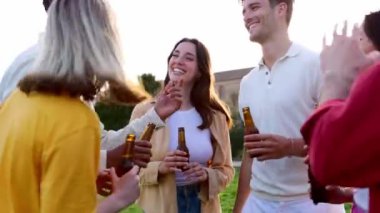 Bir grup genç arkadaş dışarıda bira şişeleriyle kutlama yapıyorlar. Çok ırklı insanlar gülerek dışarıda yaz partisinin tadını çıkarıyorlar. Topluluk, gençlik ve arkadaşlık kavramı.