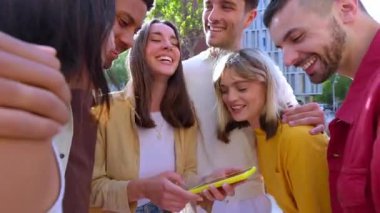 Şehir caddesinde cep telefonu kullanan bir grup mutlu genç. Milenyum çeşitliliği cep telefonu uygulamasında sosyal medyadan keyif alan arkadaşlar. Teknoloji yaşam tarzı ve gençlik toplumu kavramı.