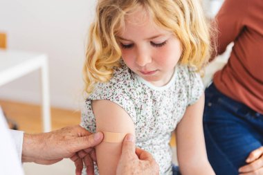 Tıbbi danışma odasındaki aşıdan sonra küçük kızın omzuna doktor yara bandı yapıştırmış. Aile hastanesinde enjeksiyondan sonra çocuklara bakan sağlık görevlisi. Sağlık hizmeti kavramı