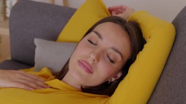 Evdeki kanepede dinlenen güzel bir kadının yakın plan portresi. Çekici, gözleri kapalı, kanepede dinlenen, hayal kuran ya da serbest günün tadını çıkaran bir kadın. Refah yaşam tarzı konsepti.