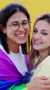 Sarı arka planda öpüşen iki güzel lezbiyen çiftin dikey portresi. LGBT halkı ve gay onur festivali konsepti.