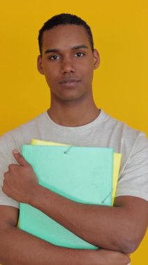 Akademik dosya klasörünü sarı arka planda tutan kendine güvenen genç çocuğun dikey video portresi. Eğitim yaşam tarzı kavramı.