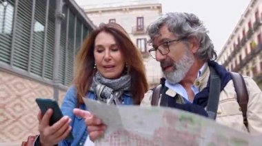 Barselona 'da yürüyüşün tadını çıkarırken elinde şehir haritası olan mutlu yetişkin turist çifti. Evli, orta yaşlı bir adam ve kadın seyahat sırasında telefon uygulamasından turistik konum arıyorlar..