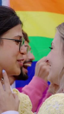 Arka planda eşcinsel onur ayı festivalini kutlayan LGBT arkadaş grubuyla öpüşen iki genç kadının dikey HD 'si. Lezbiyen ve eşcinseller LGBTQ partisinde eğleniyorlar.. 