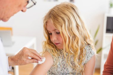 Hastane odasındaki küçük kıza kıdemli erkek doktor aşı yapıyor. Çocuk sağlığı konsepti.