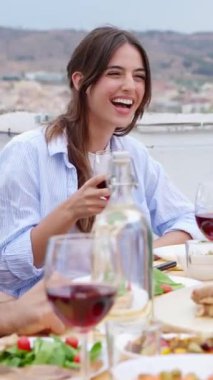 Çeşitli arkadaşların çatıdaki partide yemek yediği bir grup gülümsemenin dikey videosu. Mutlu bin yıllık çok ırklı insanlar gülerek ve eğlenerek yaz kutlamalarında masada oturuyorlar..