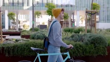 Bisikletle kampüsten ayrılan mutlu genç öğrenci. Eğitim, insanlar ve çevre dostu ulaşım kavramı. Yan görünüm.