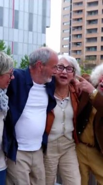 Emekli bir grup emeklinin şehir caddesinde yürürken birbirlerine sarılırken eğlendikleri dikey HD videoları. Emeklilik ve yaşlılık arkadaşlık kavramı.